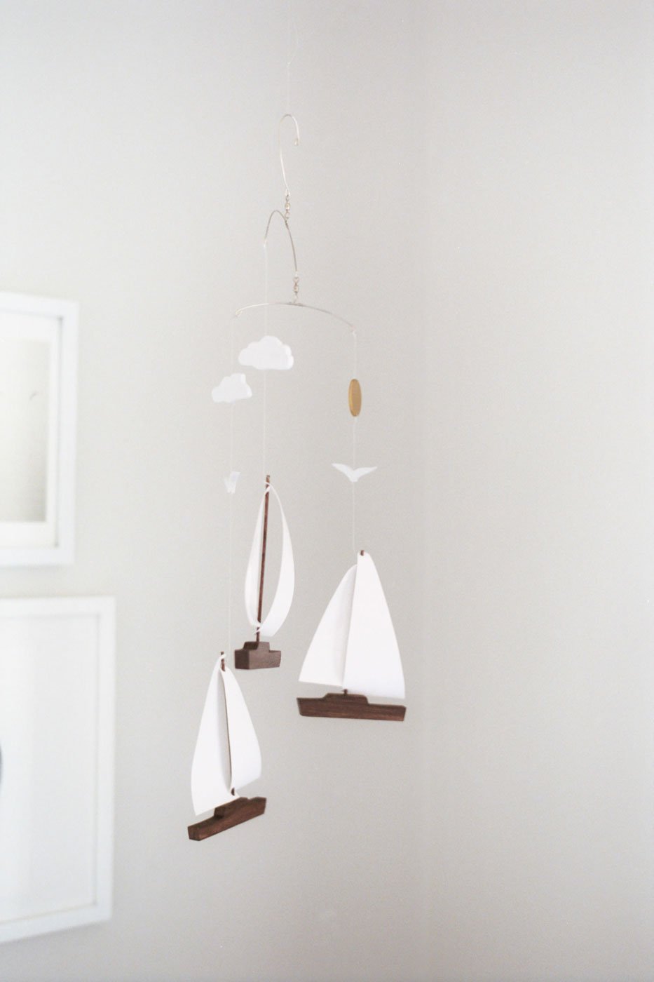 Decorative hanging mobile with white sailboats, clouds, and birds, against a plain light-colored wall.