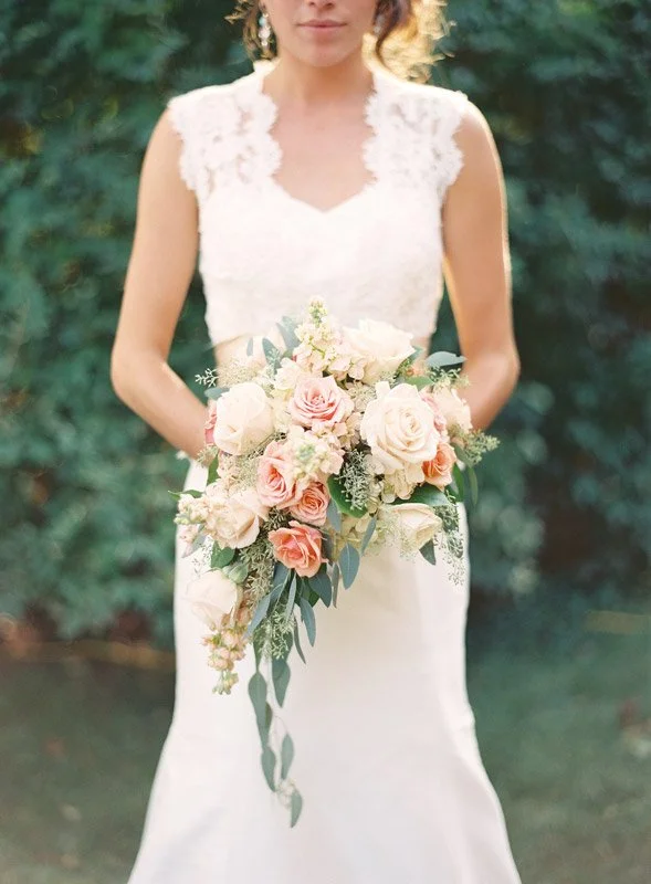 Bride holding a cascading bouquet of pink and white roses with greenery outdoors.