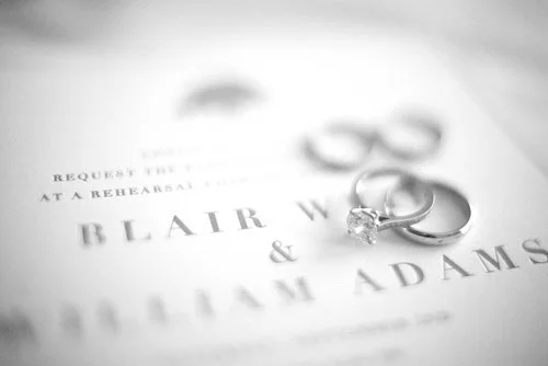 Wedding rings placed on a wedding invitation for Blair W. and William Adams.