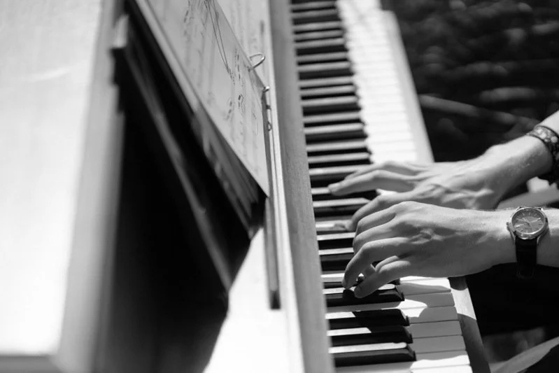 Black and white photo of a person's hands playing the piano, with sheet music on the stand.