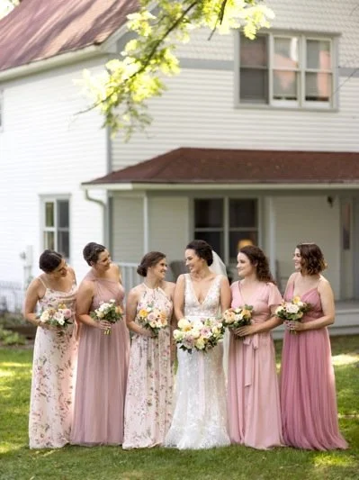 Bride in white dress with six bridesmaids in pink dresses outdoors in front of a house.