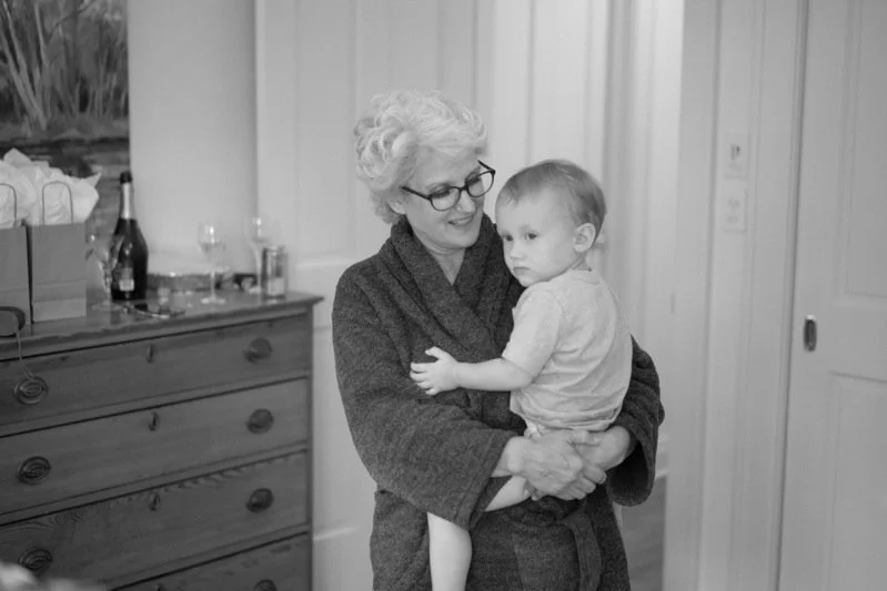 An elderly woman with glasses and curly white hair holding a young child in a cozy room.