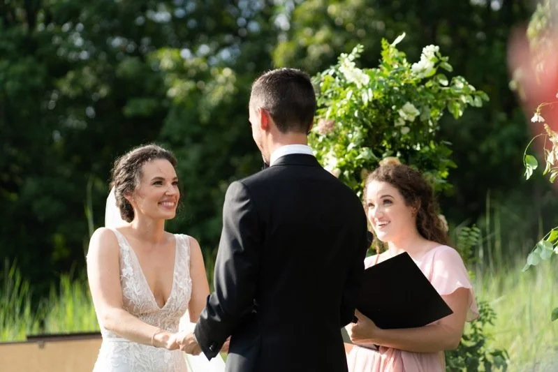 A bride and groom exchange vows outdoors with an officiant.