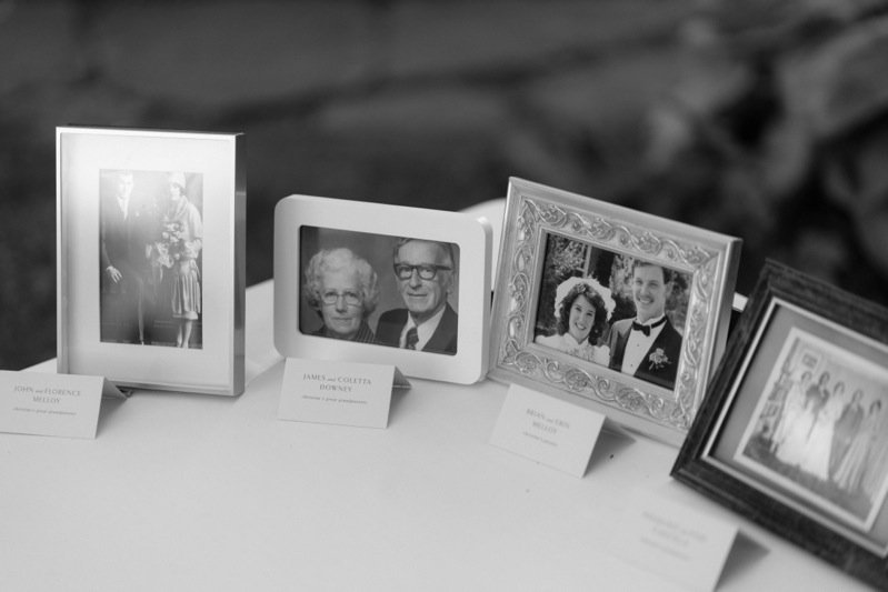 A display of four framed photographs on a table, including family portraits and black-and-white images, with small labels in front of each frame.