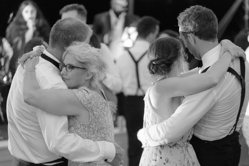 Couples dancing closely at a formal event, with one woman wearing glasses and a sparkly dress, and another woman with her hair in a bun, all in black and white.