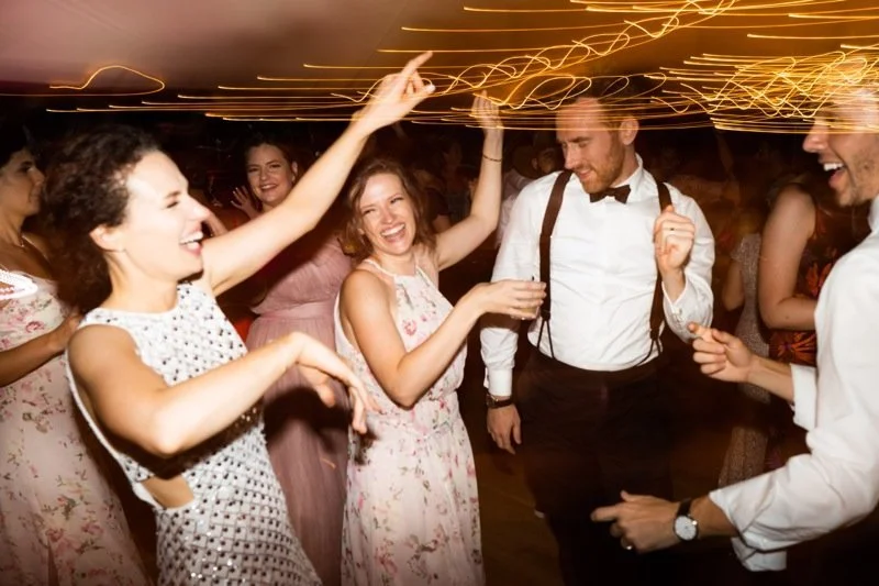 Group of people dancing and celebrating at a party, with colorful lights and joyful expressions.