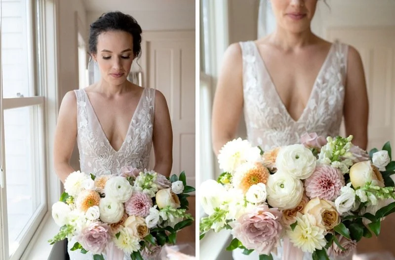 A woman in a lace wedding dress holding a large bouquet of pastel-colored flowers indoors.