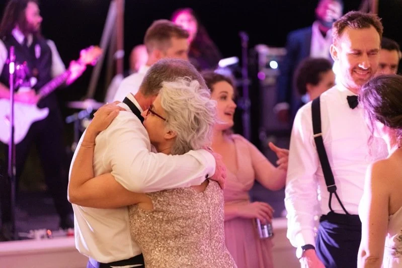 People dancing and embracing at a celebration with a live band playing in the background.