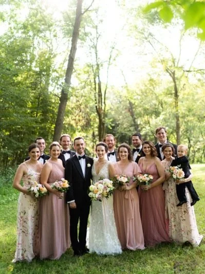 Group of people at a wedding outdoors in a wooded area, including a bride and groom, bridesmaids, and children.