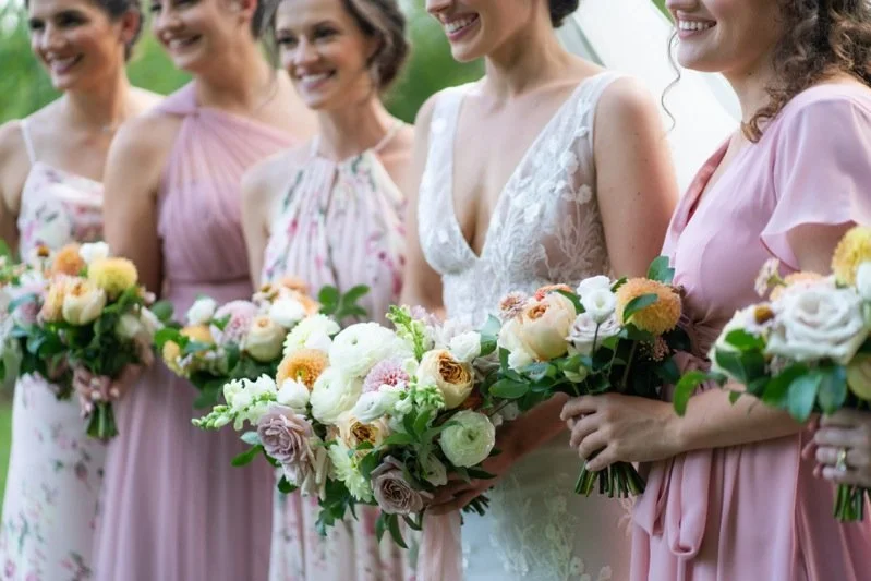 Group of women in colorful dresses holding bouquets at a wedding ceremony.