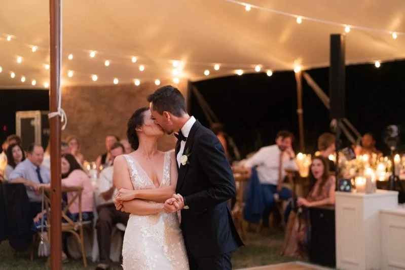 Bride and groom sharing their first dance at a wedding reception, surrounded by seated guests and string lights overhead.