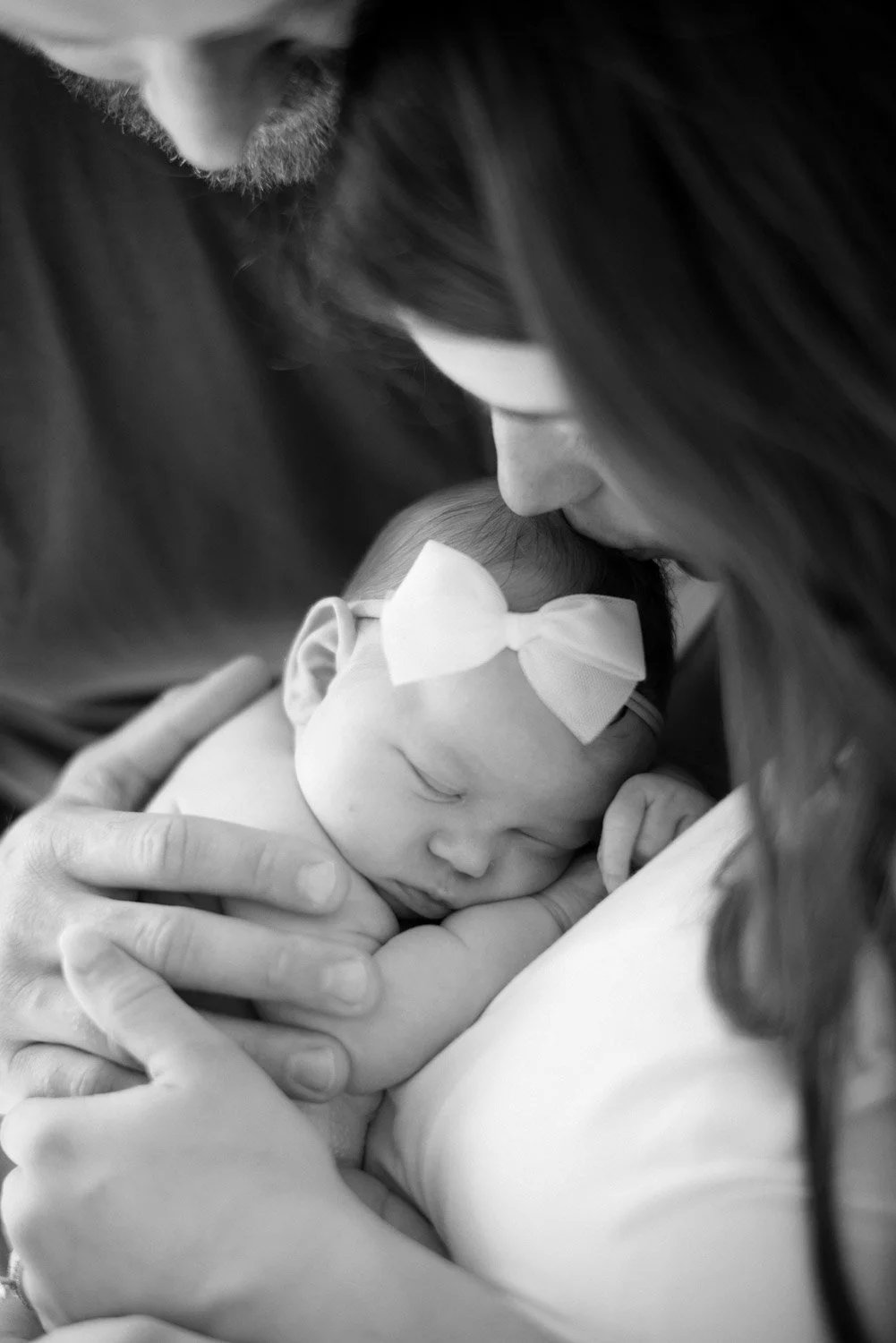 Black and white photo of a woman gently holding a newborn baby with a bow in the baby's hair, who is sleeping peacefully.