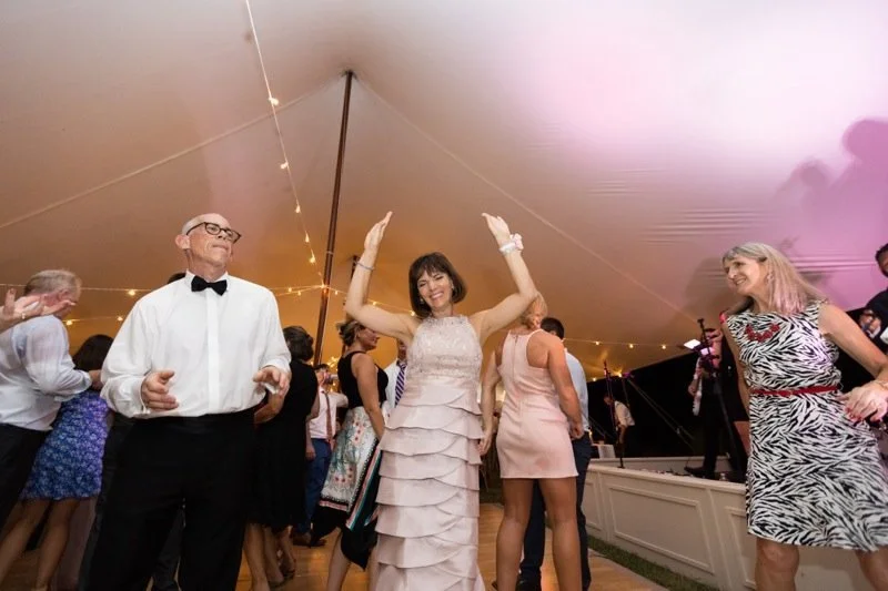People dancing and enjoying themselves at a party inside a large tent with string lights.