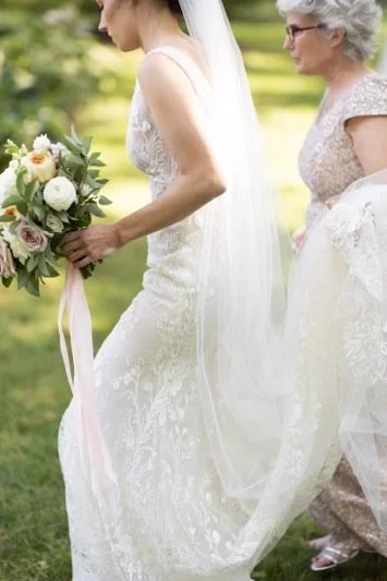 A bride holding a bouquet and an older woman in a garden setting.
