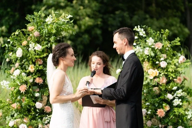 Bride and groom exchanging vows during outdoor wedding ceremony with floral arch in the background.