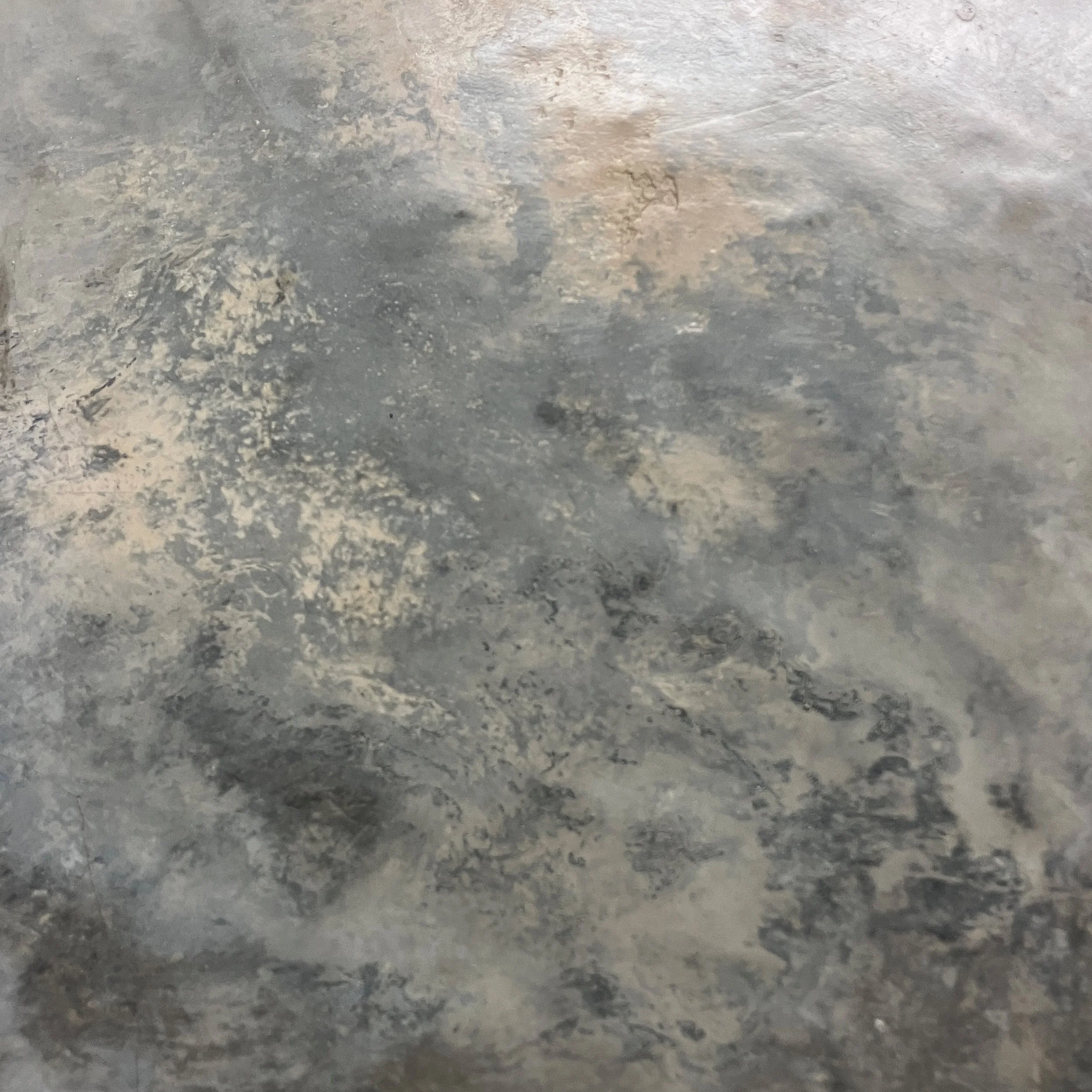 Close-up of a metallic, textured surface with various shades of gray, silver, and beige, showing scratches, patches, and irregular patterns.