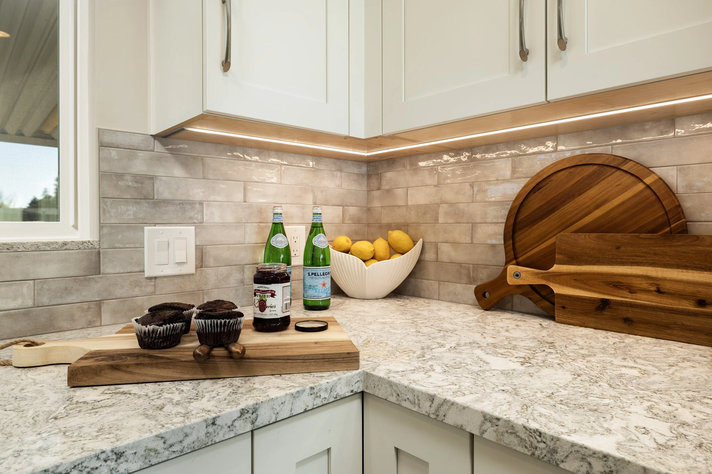 Transitional kitchen design details featuring ceiling-height glossy subway tile, floating white shelves, and a stainless steel range hood.