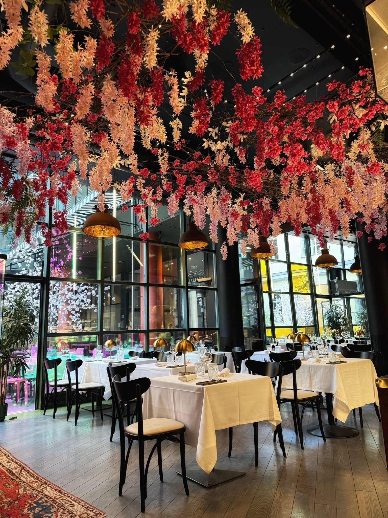 Elegant restaurant with white tablecloths, black chairs, and decorative pink and white hanging flowers from the ceiling.