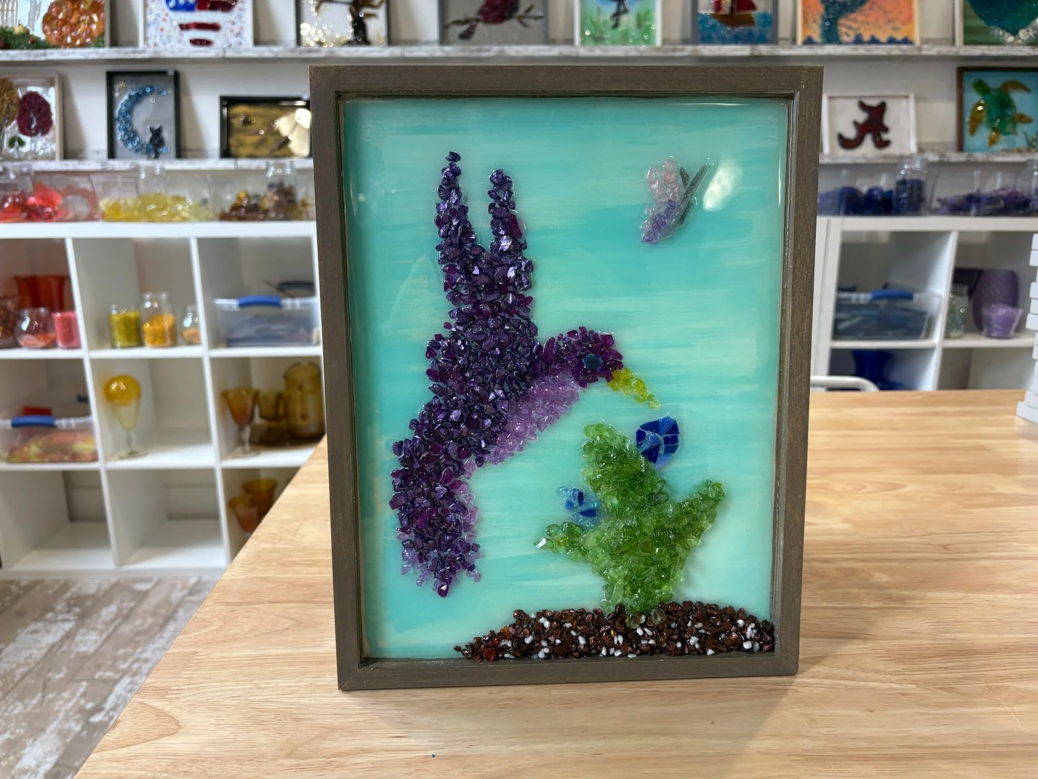 Resin Glass Art of a humming bird and flower using cut and crushed glass in a painted frame.