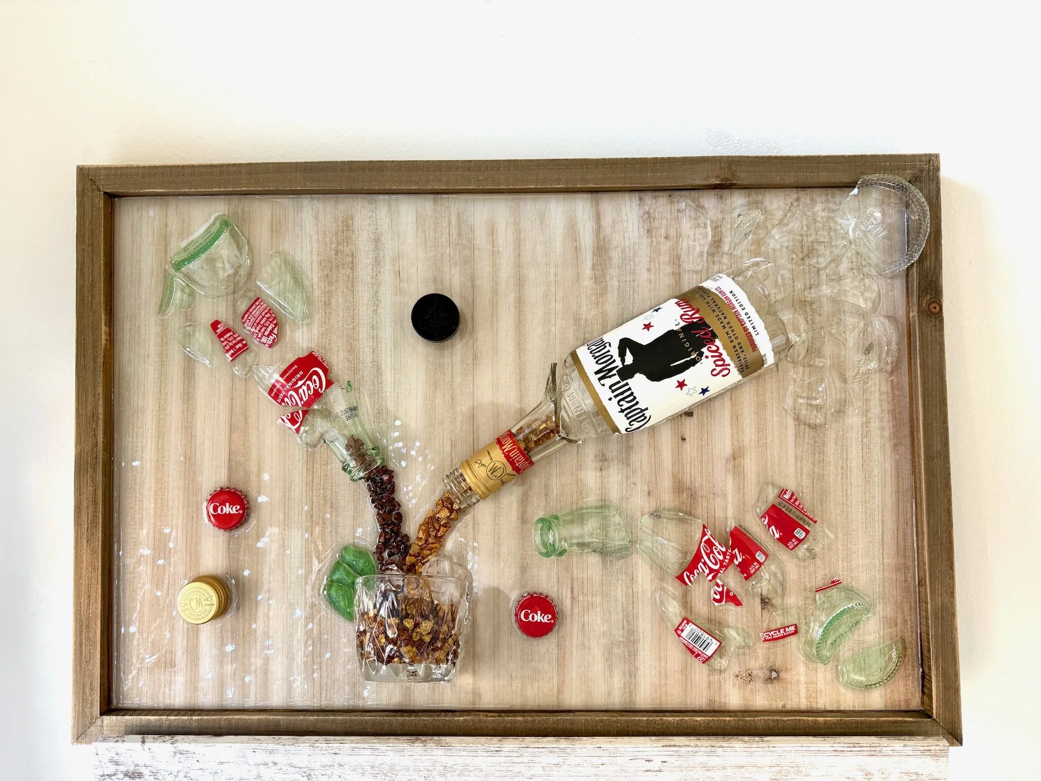 Resin Glass Art of a broken rum and coke bottles pouring into a glass of ice with lime on the side using cut and crushed glass in a painted frame. Man Cave Art.