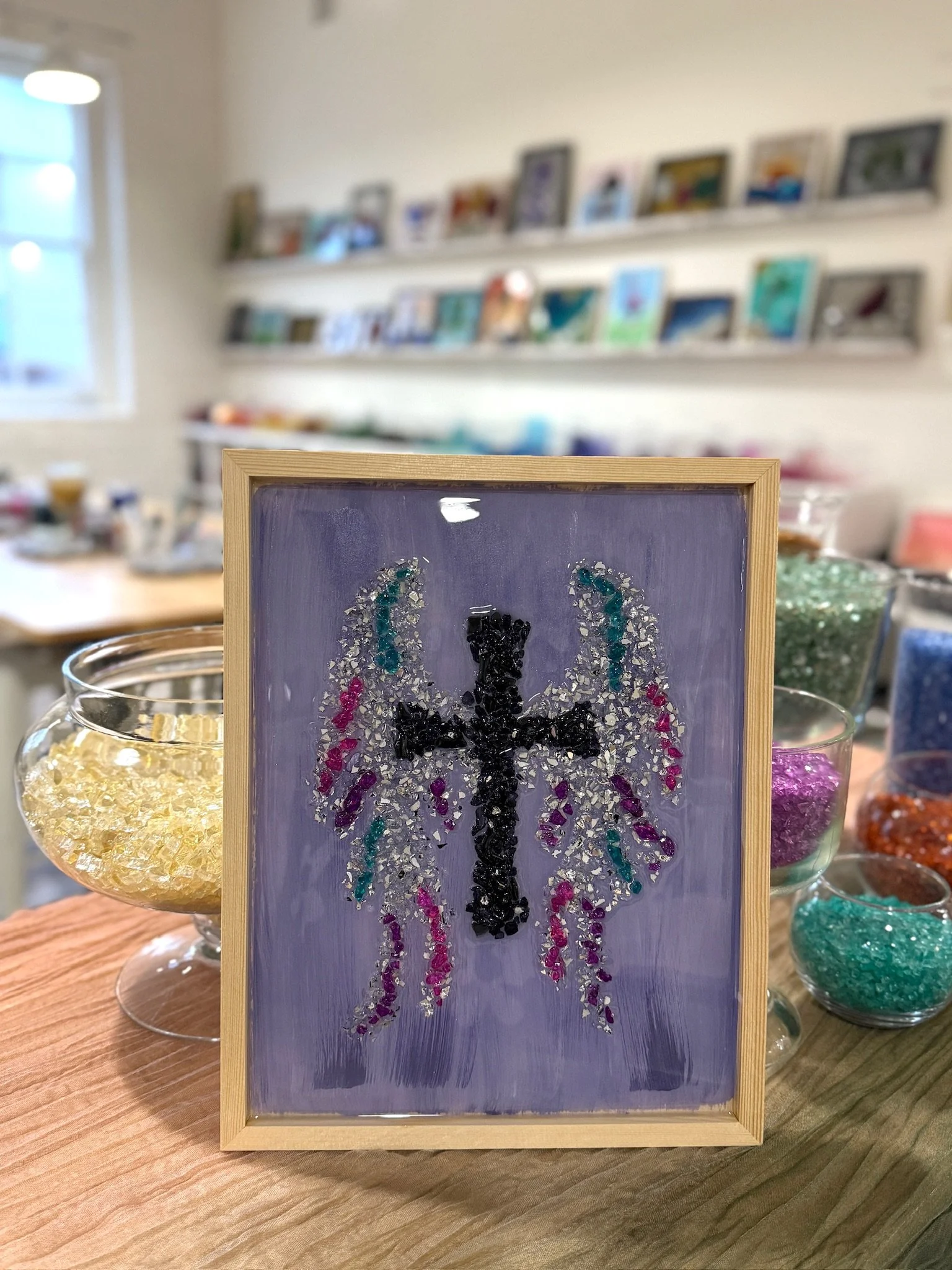 Resin Glass Art of a cross with angel wings around it using cut and crushed glass in a painted frame.