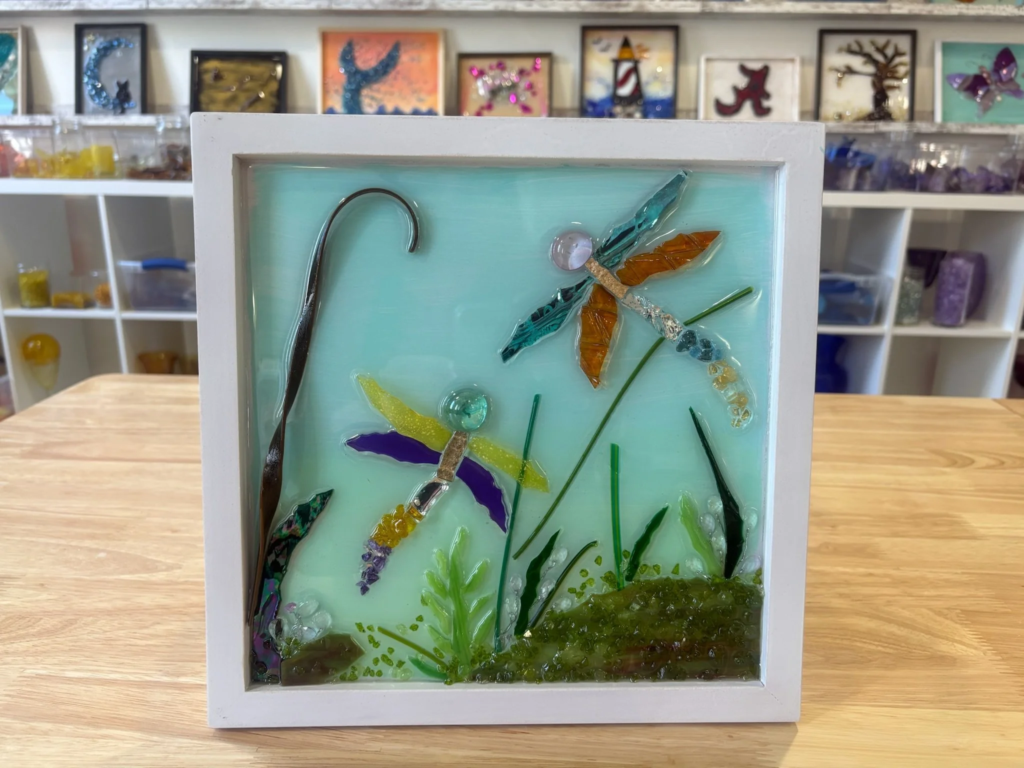 Resin Glass Art of an dragon fly's and grass close up using cut and crushed glass in a painted frame.
