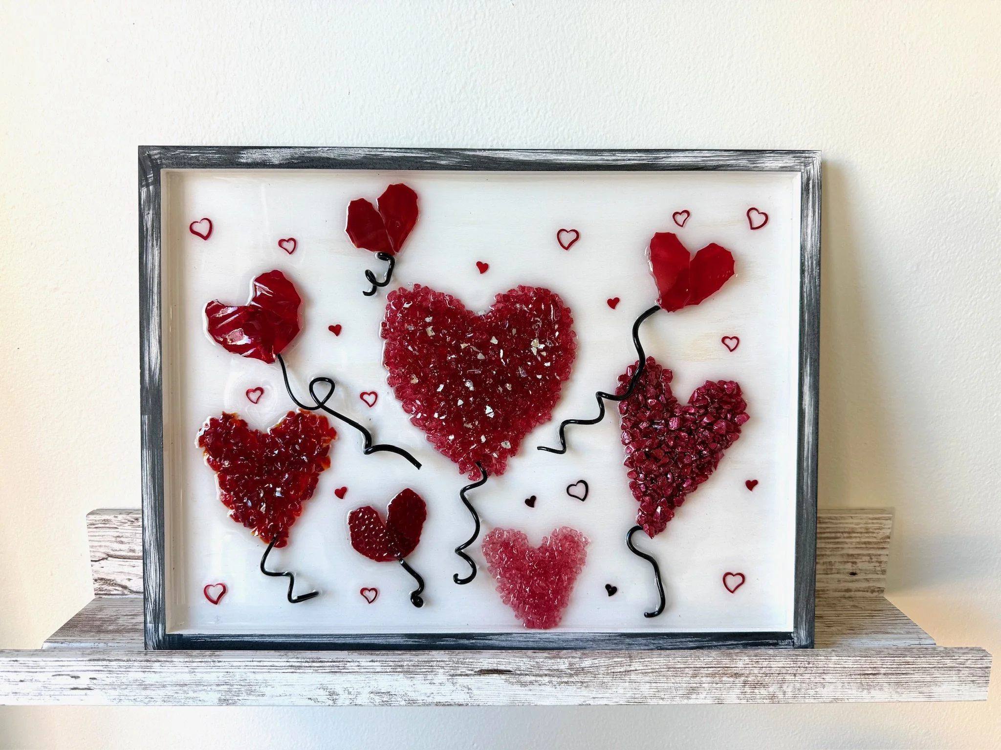 Framed Valentine's resin artwork featuring various red hearts made of different textured materials, with black curly wires and small red heart drawings scattered around on a white background.