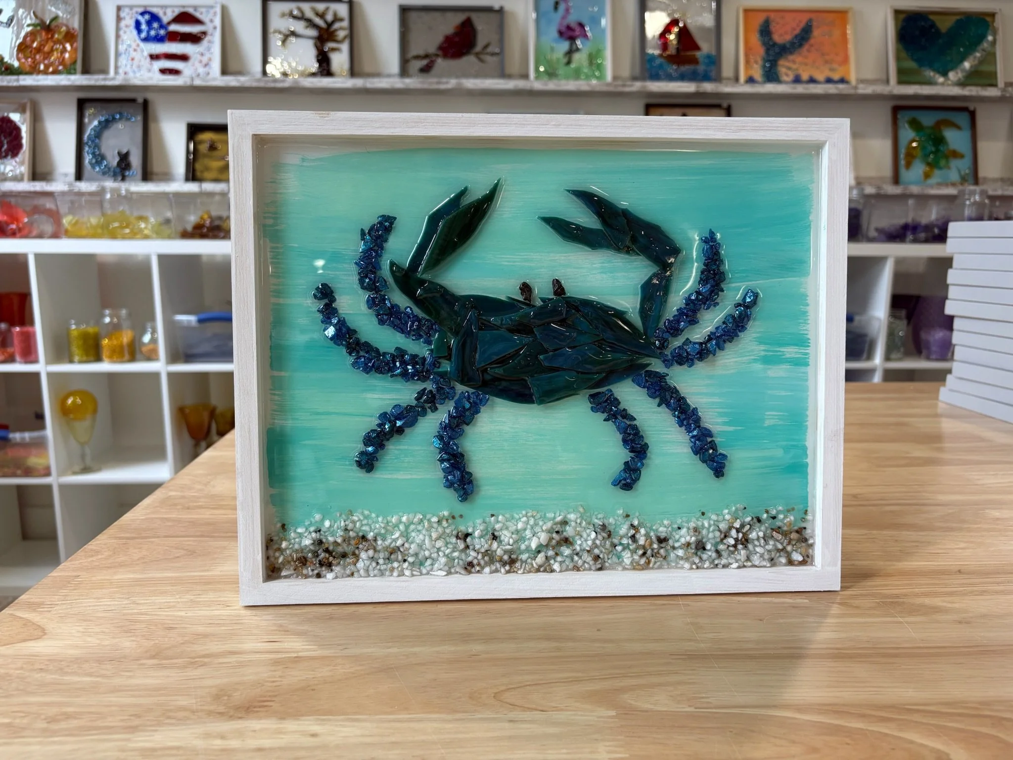 Resin Glass Art of a crab and the ocean floor using cut and crushed glass in a painted frame.