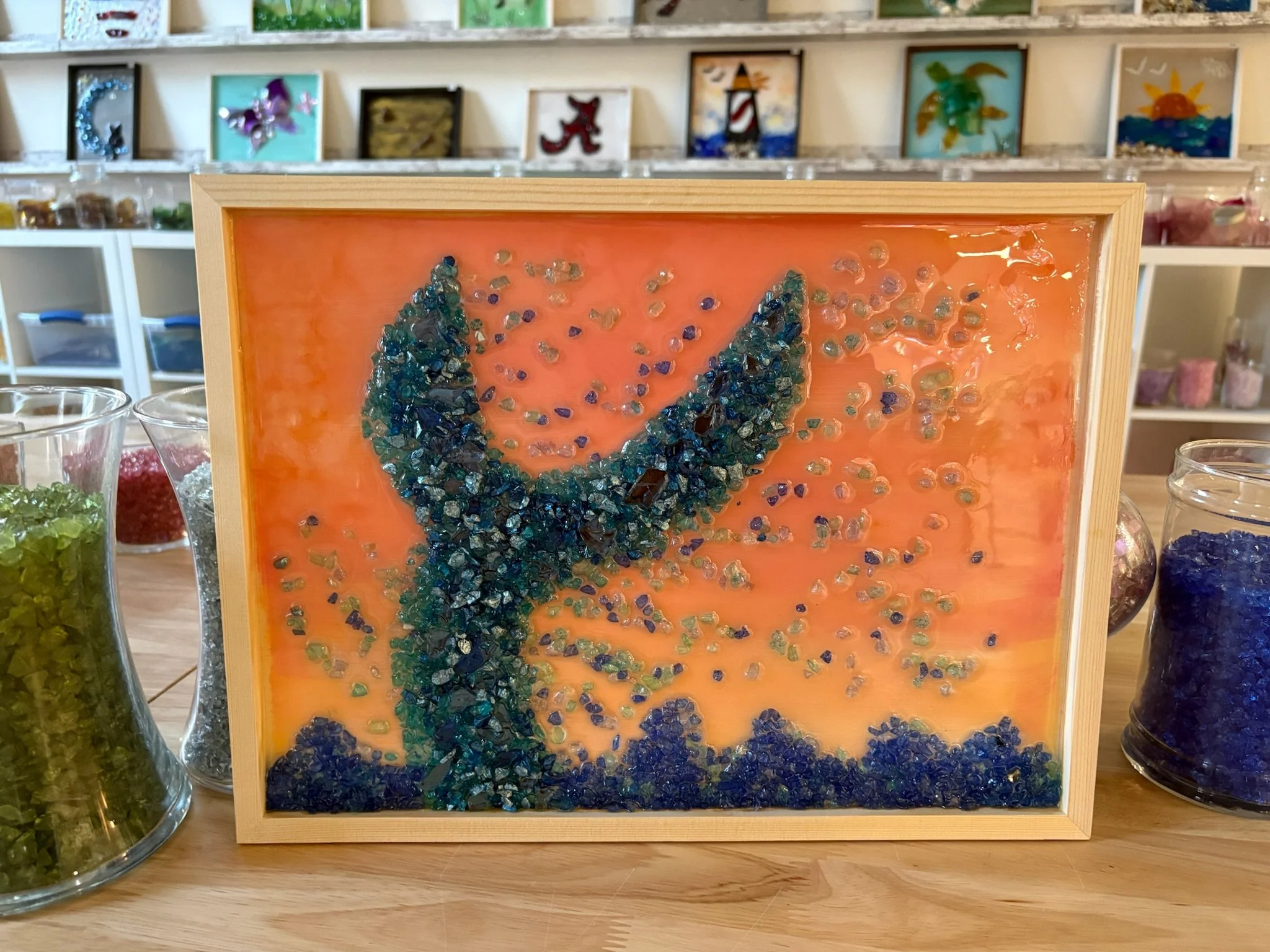 Resin Glass Art of whale tale splashing in the ocean and water falling off of it using cut and crushed glass in a painted frame.