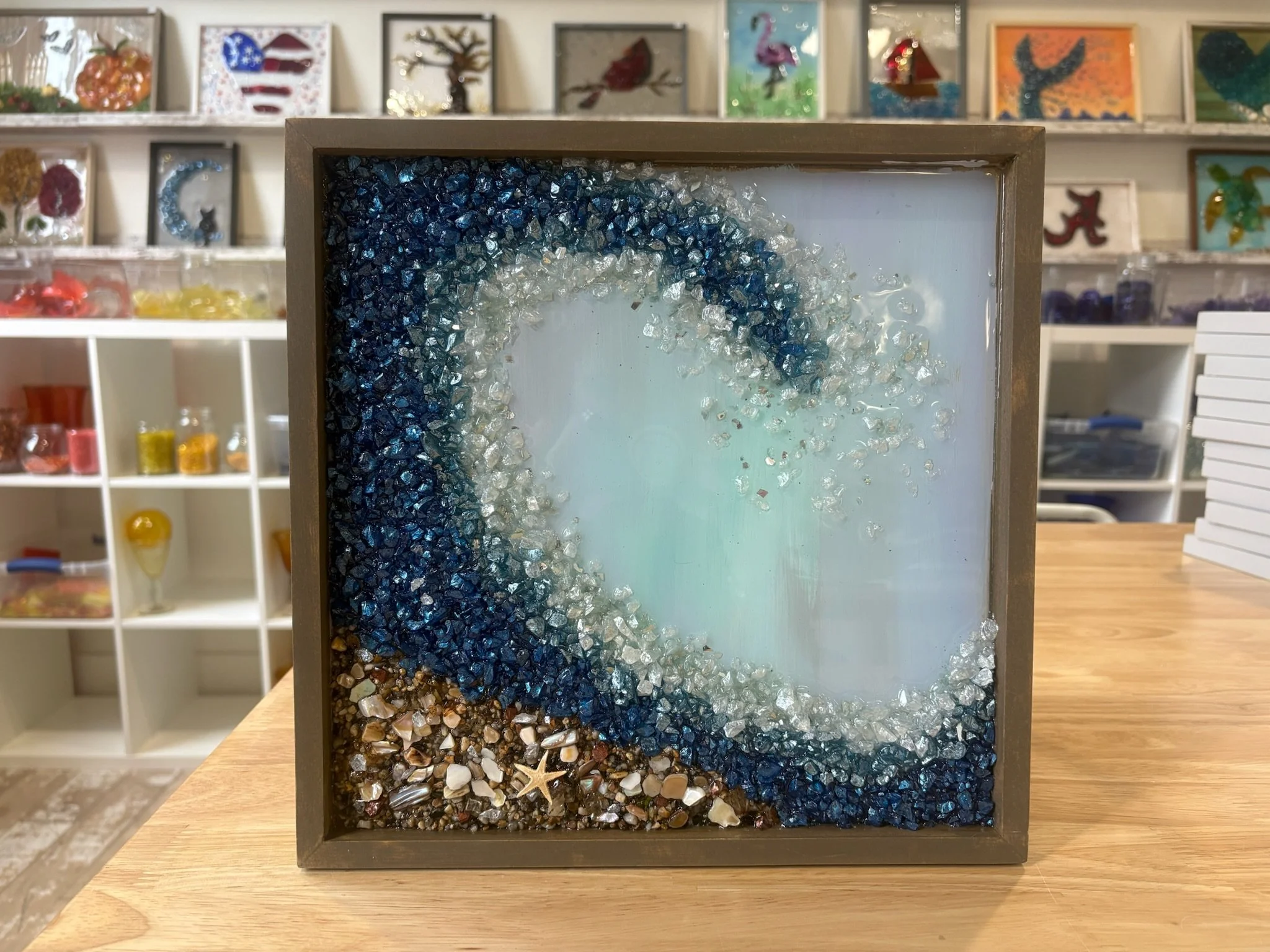 A framed resin  art piece depicting a beach scene with a starfish and pebble beach.