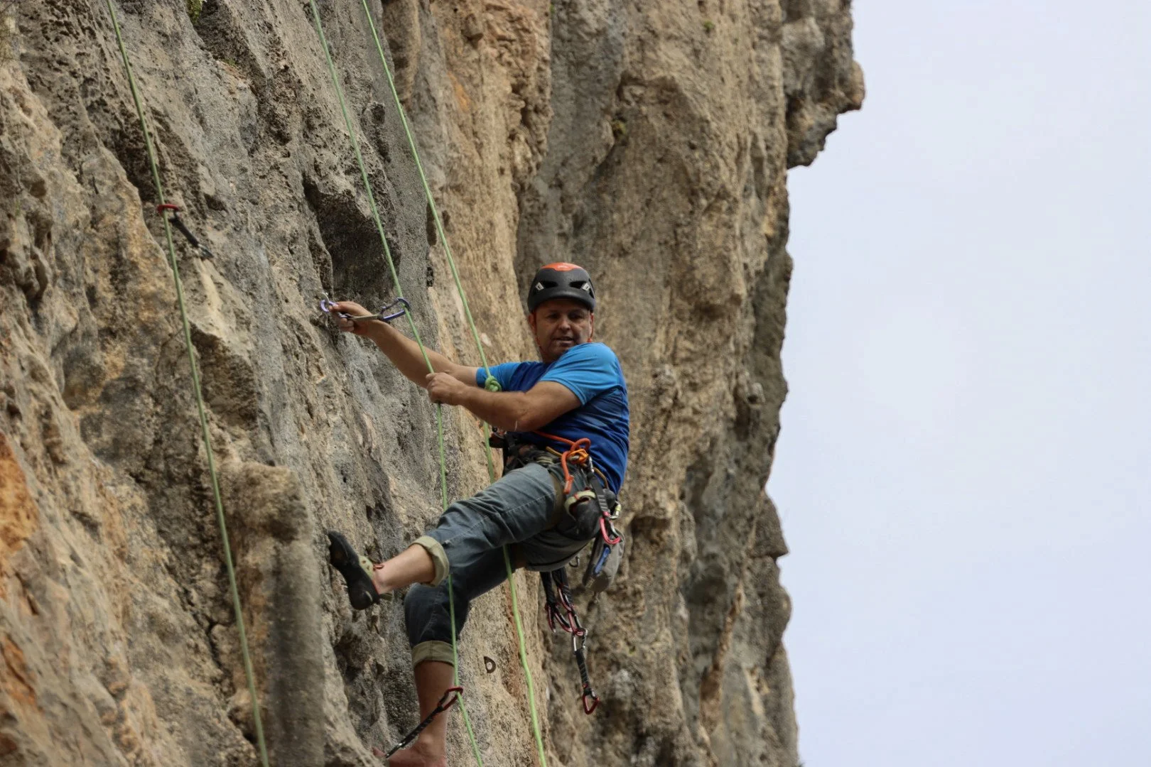 A man wearing a helmet and climbing gear is climbing a steep rock wall using ropes and safety equipment.