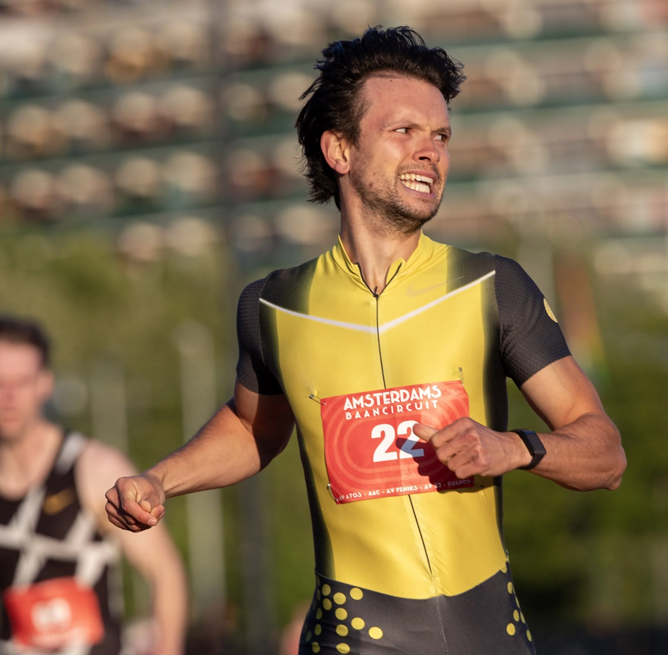 A male marathon runner in a yellow and black athletic uniform, wearing a bib number 22, participating in a race during daytime, with a focused expression on his face.