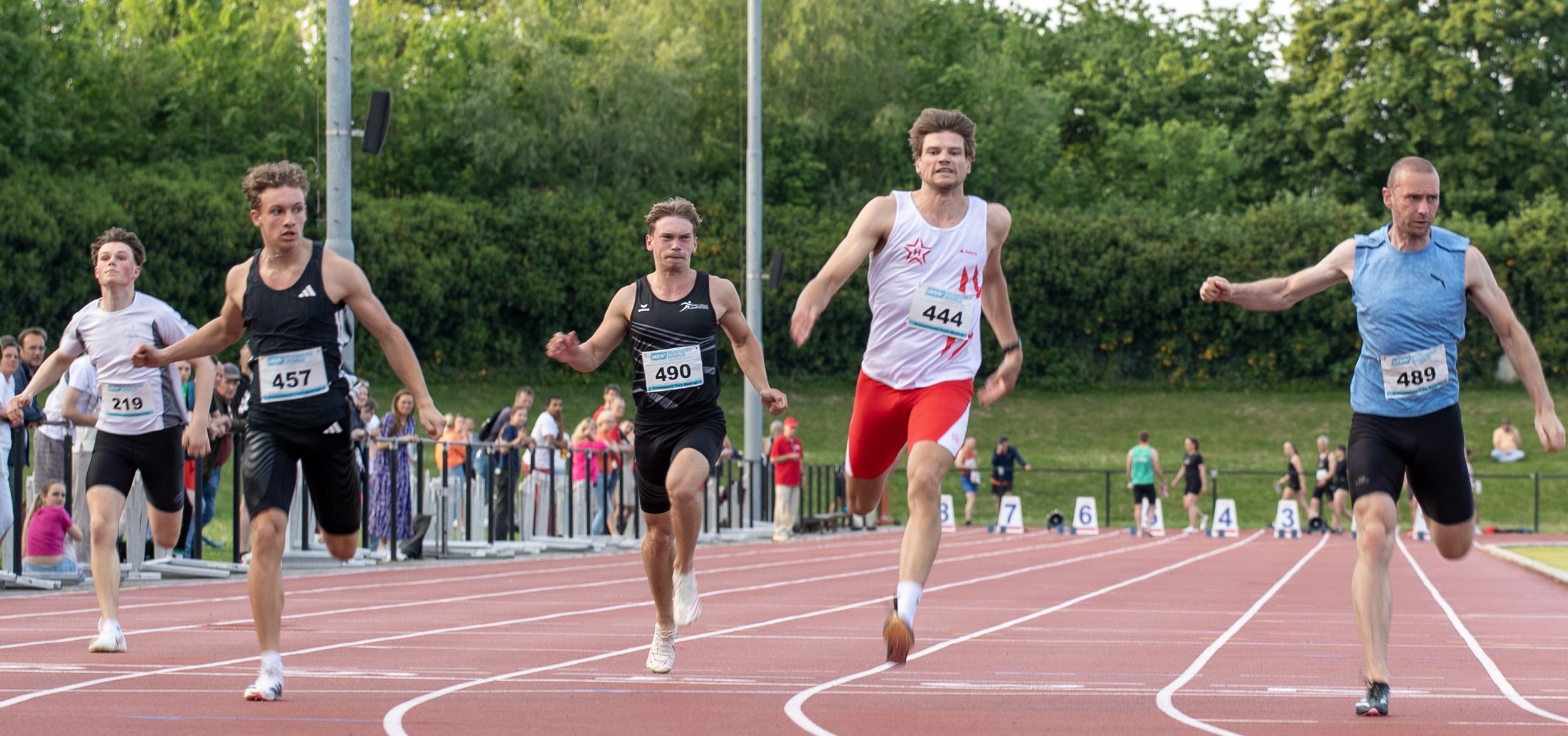Male runners competing in a track race, with spectators in the background.