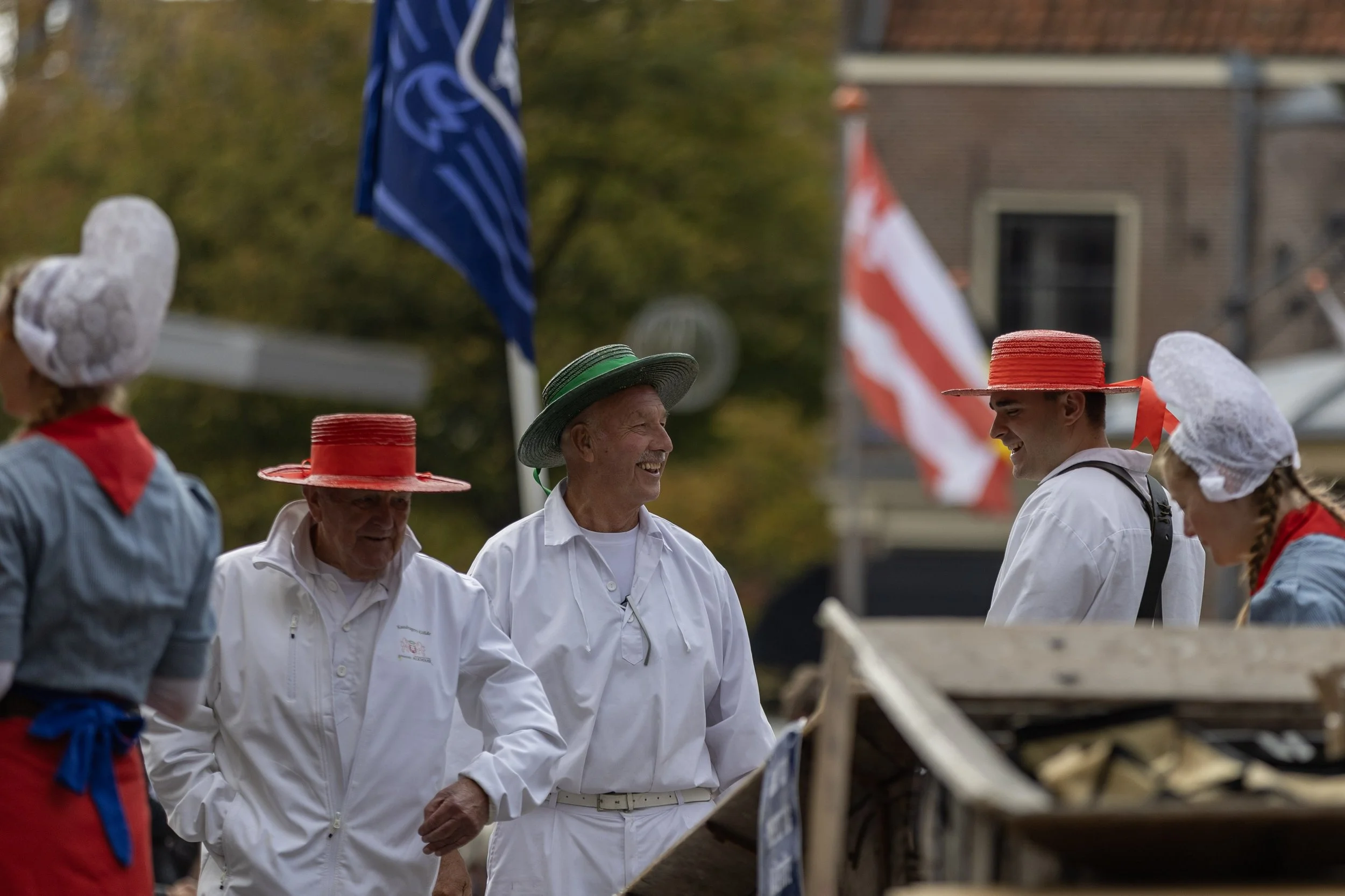 group of people wearing historical clothing and hats, standing outdoors at a parade or festival, with American flags in the background