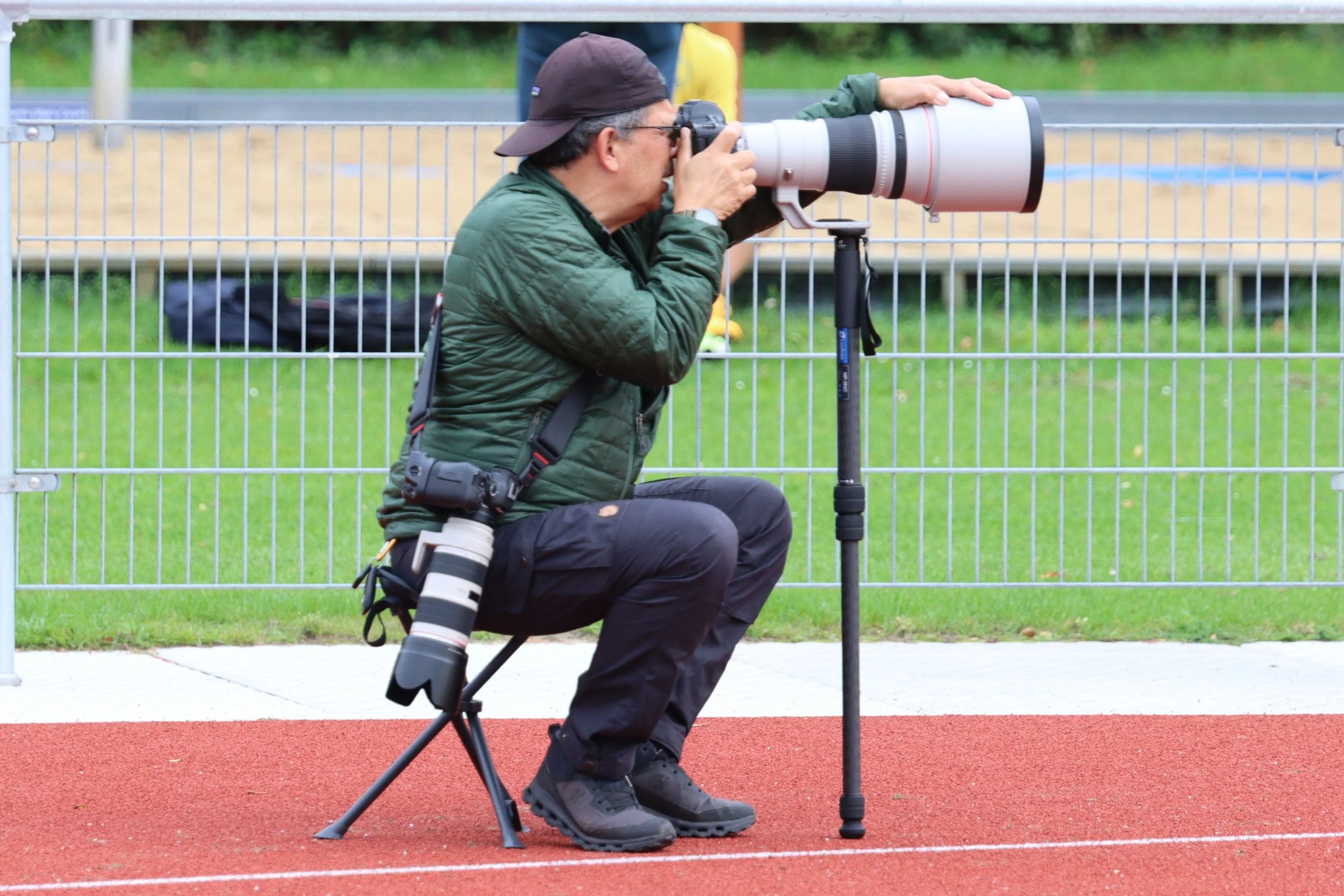 Photographer with a long telephoto lens taking pictures at a sports event on a track field.