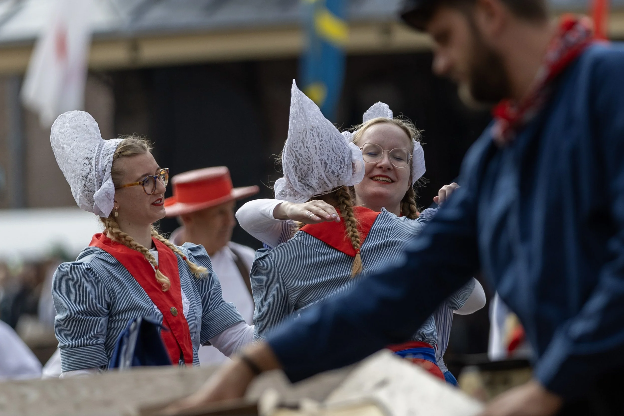 People dressed in traditional European folk costumes, including women with lace bonnets and braided hair, at an outdoor event or festival.