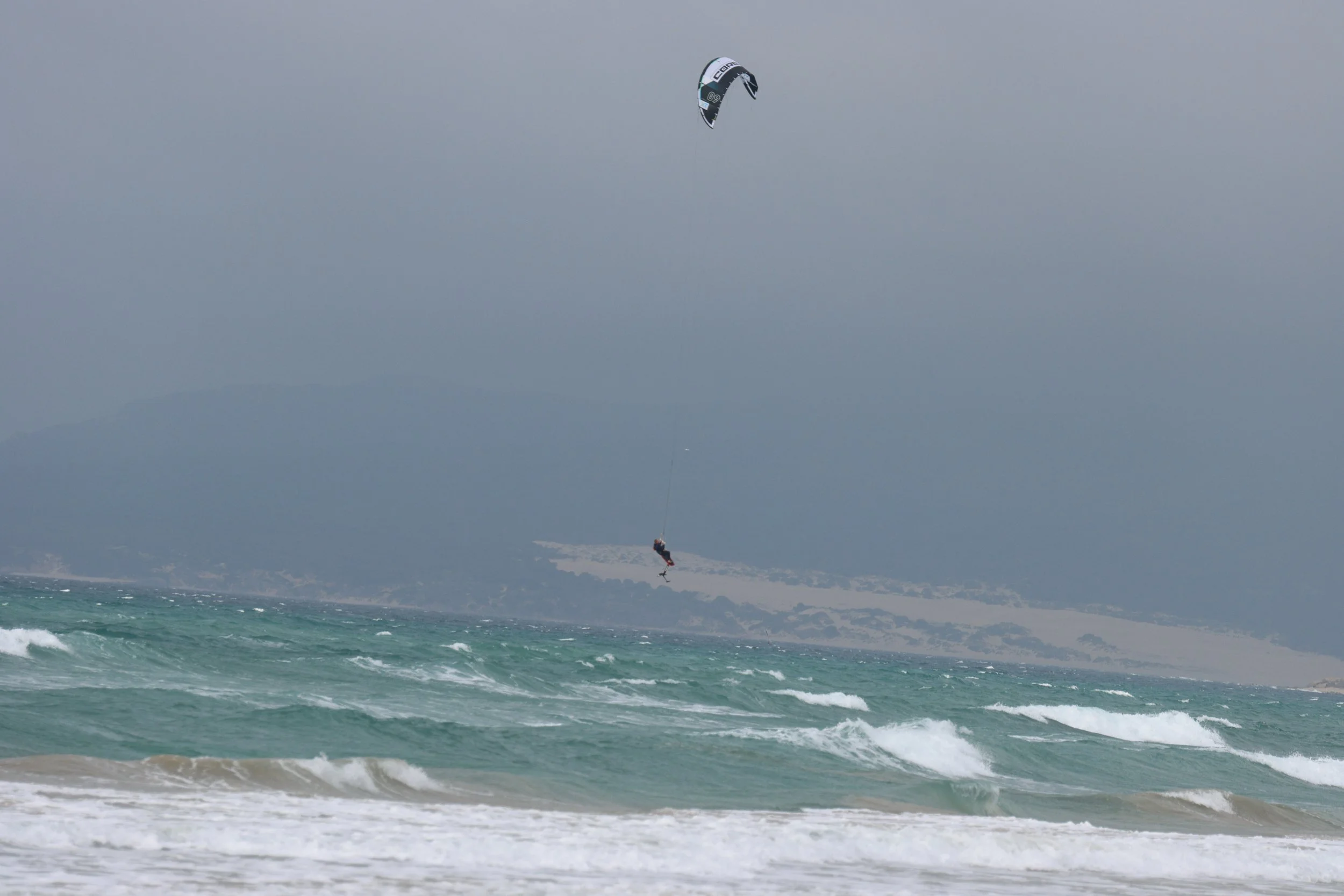 A kite surfer gliding over ocean waves under a cloudy sky.