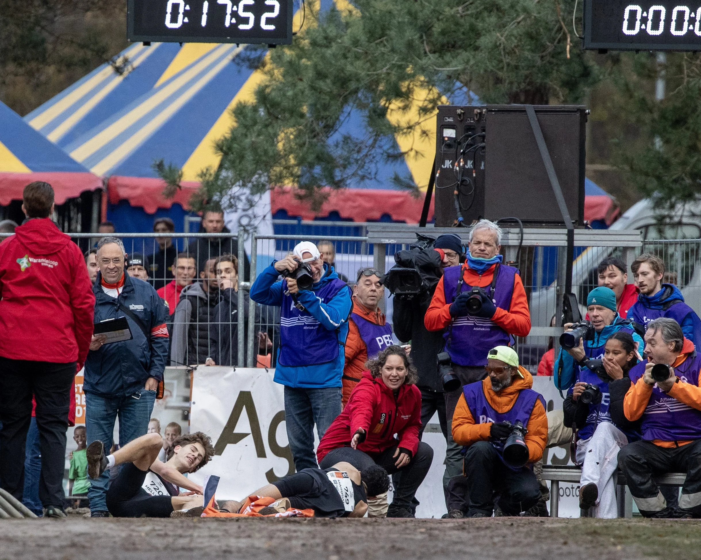 Crowd of runners and spectators at a finish line of a race, with timing clocks in the background displaying elapsed time.