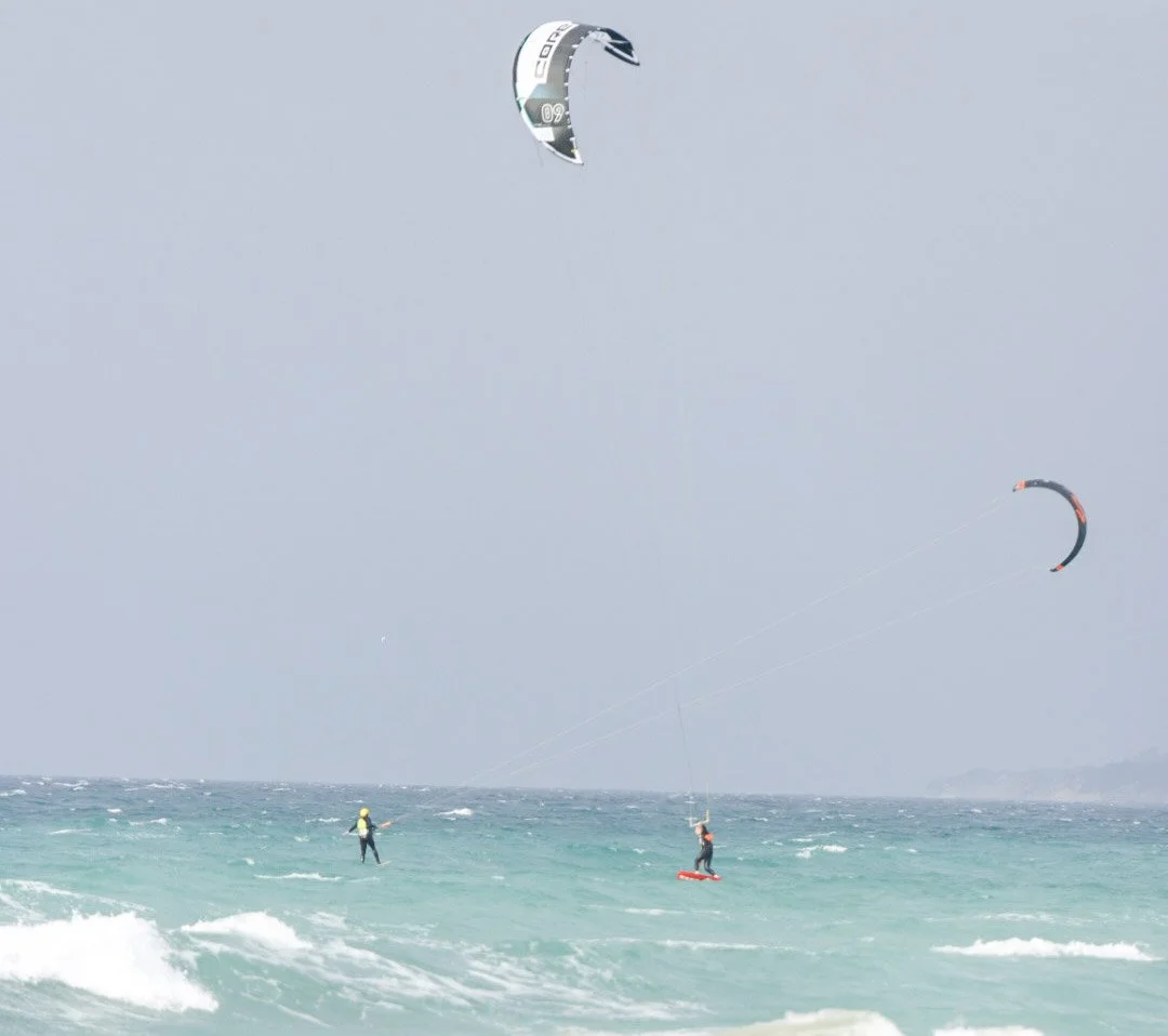 People kite surfing in the ocean with two large kites flying in the sky.