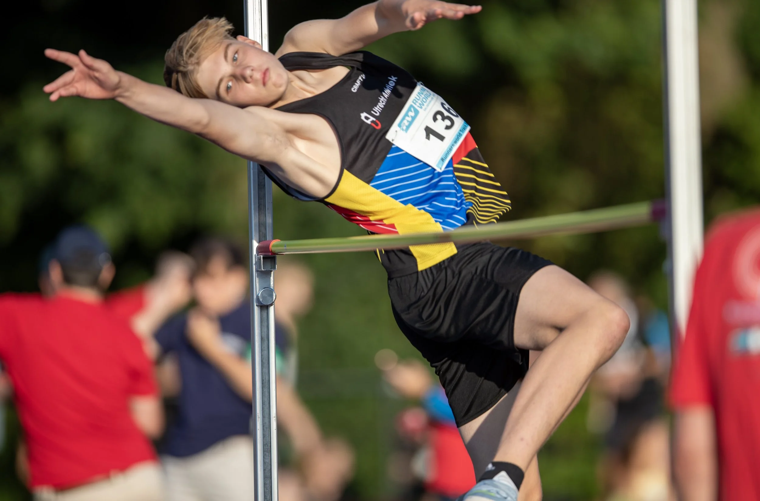 Young male athlete in colorful sportswear attempts to clear the high jump bar at a track and field event.