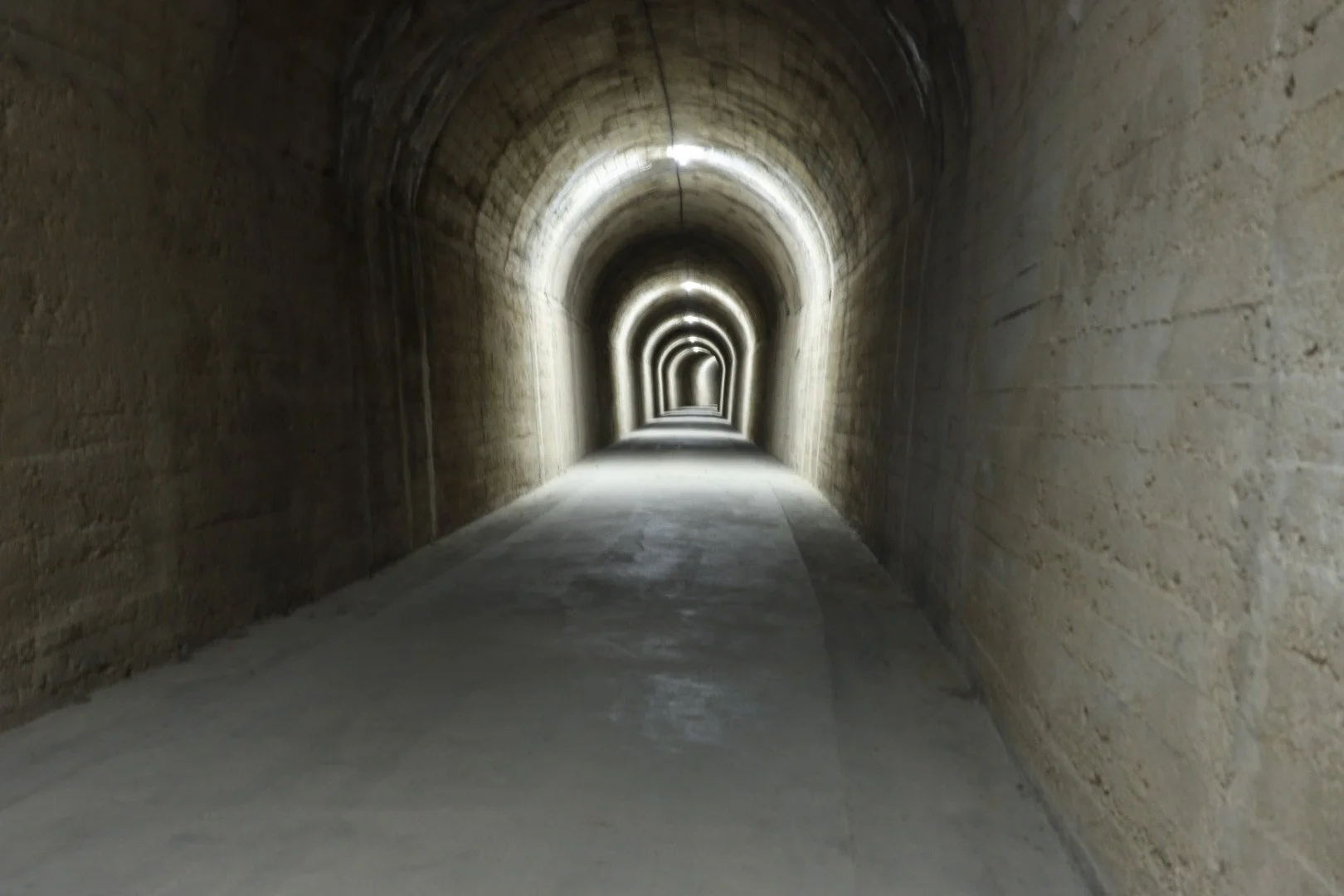 A long underground tunnel with arched ceilings, illuminated by lights along the top edges, with a smooth concrete floor.