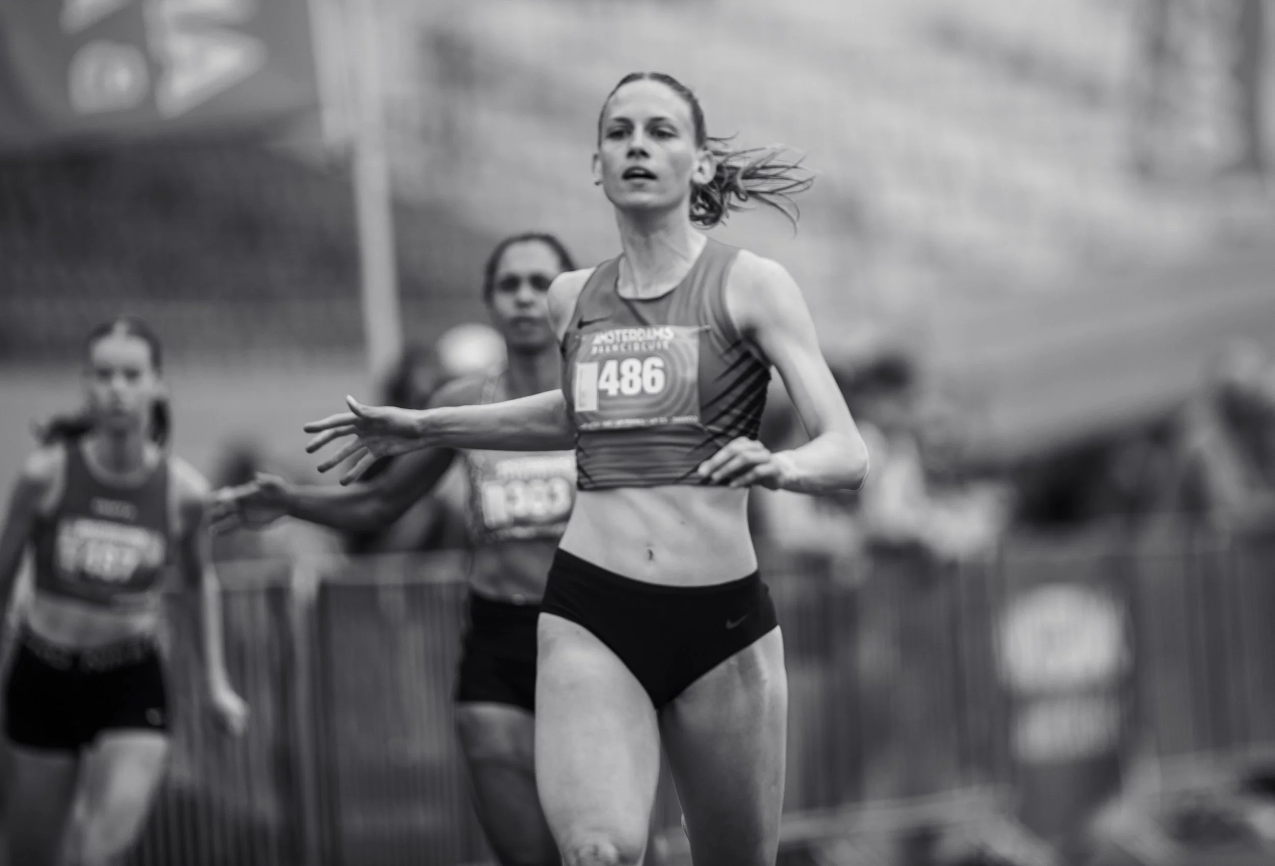 A female runner with a bib number 486 competing in a race, surrounded by other runners, with a focused expression.