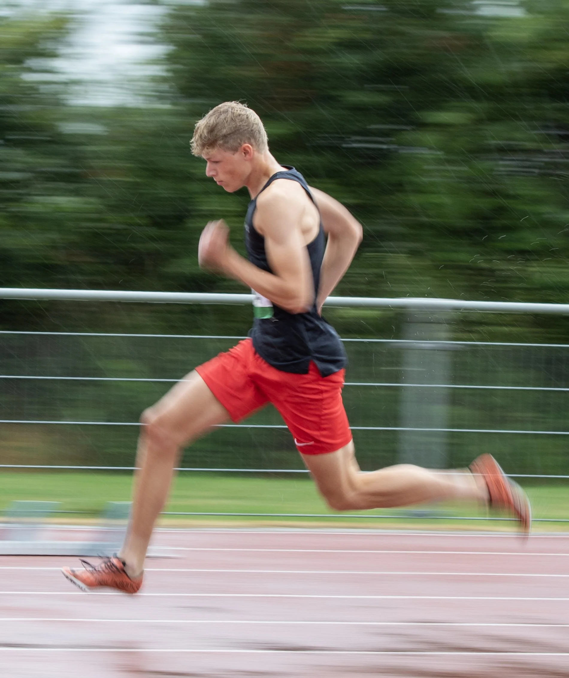 Young male athlete running on a track during rainy weather