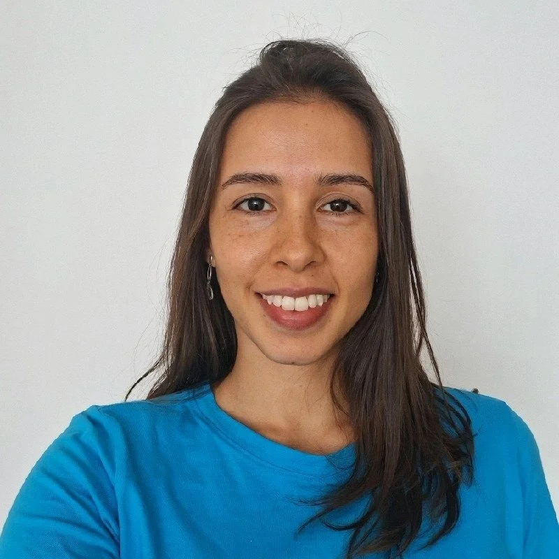 Mulher sorridente com cabelo castanho escuro, usando camiseta azul, em fundo branco