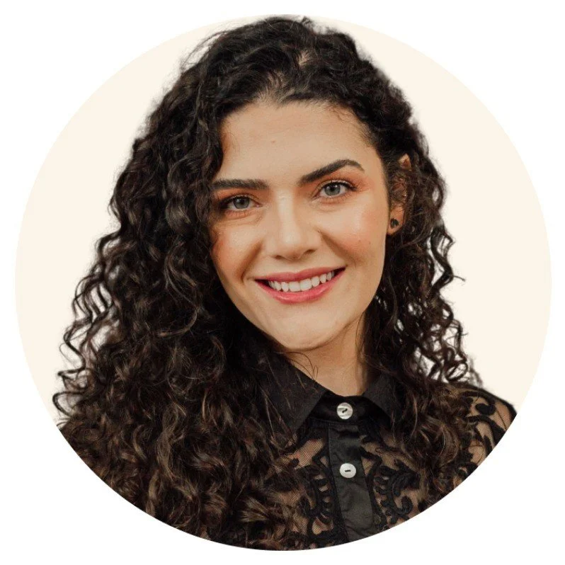 Mulher com cabelos cacheados escuros e sorriso, usando blusa preta com detalhes de renda