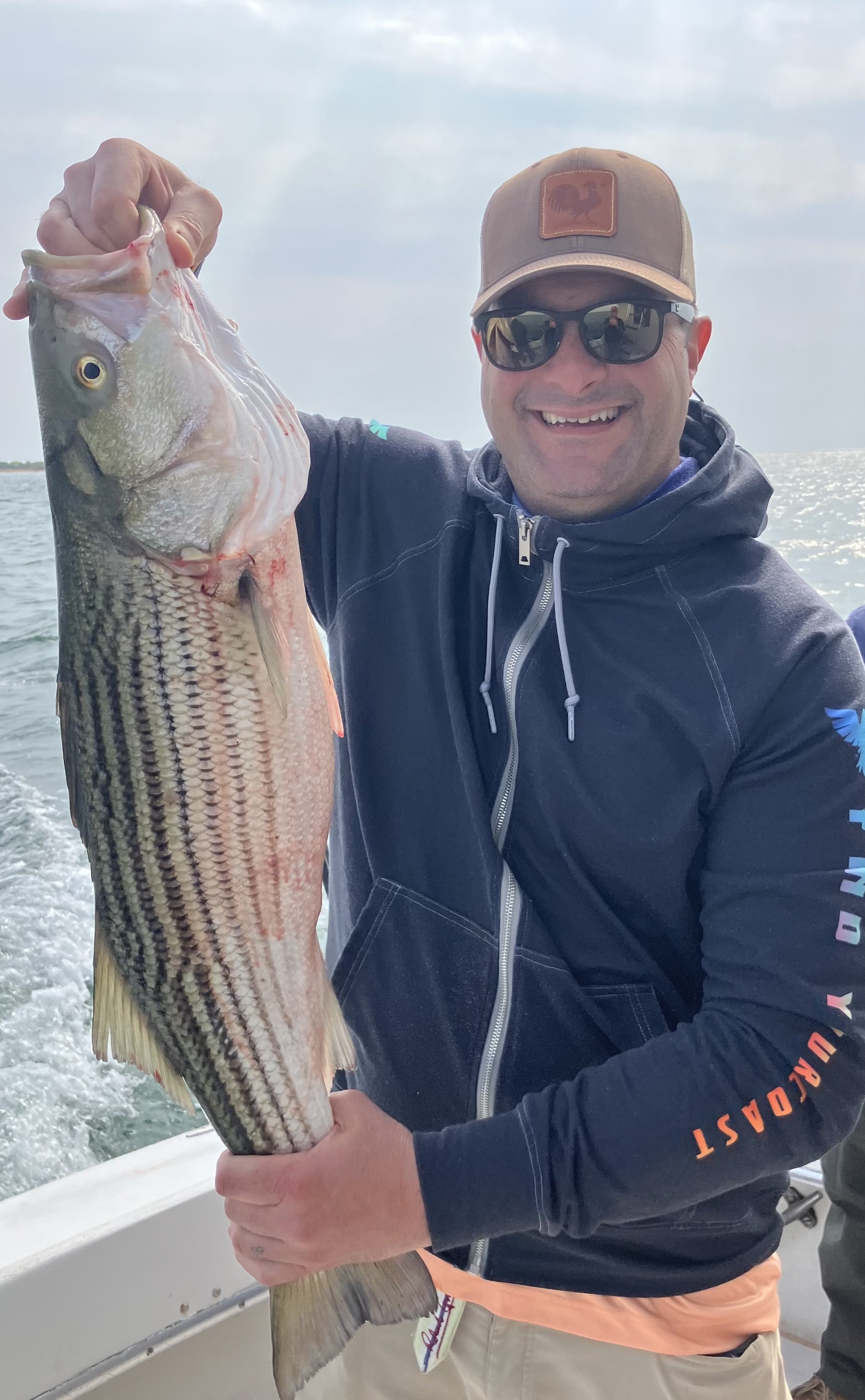 A smiling man wearing sunglasses and a cap holding a large fish on a boat.