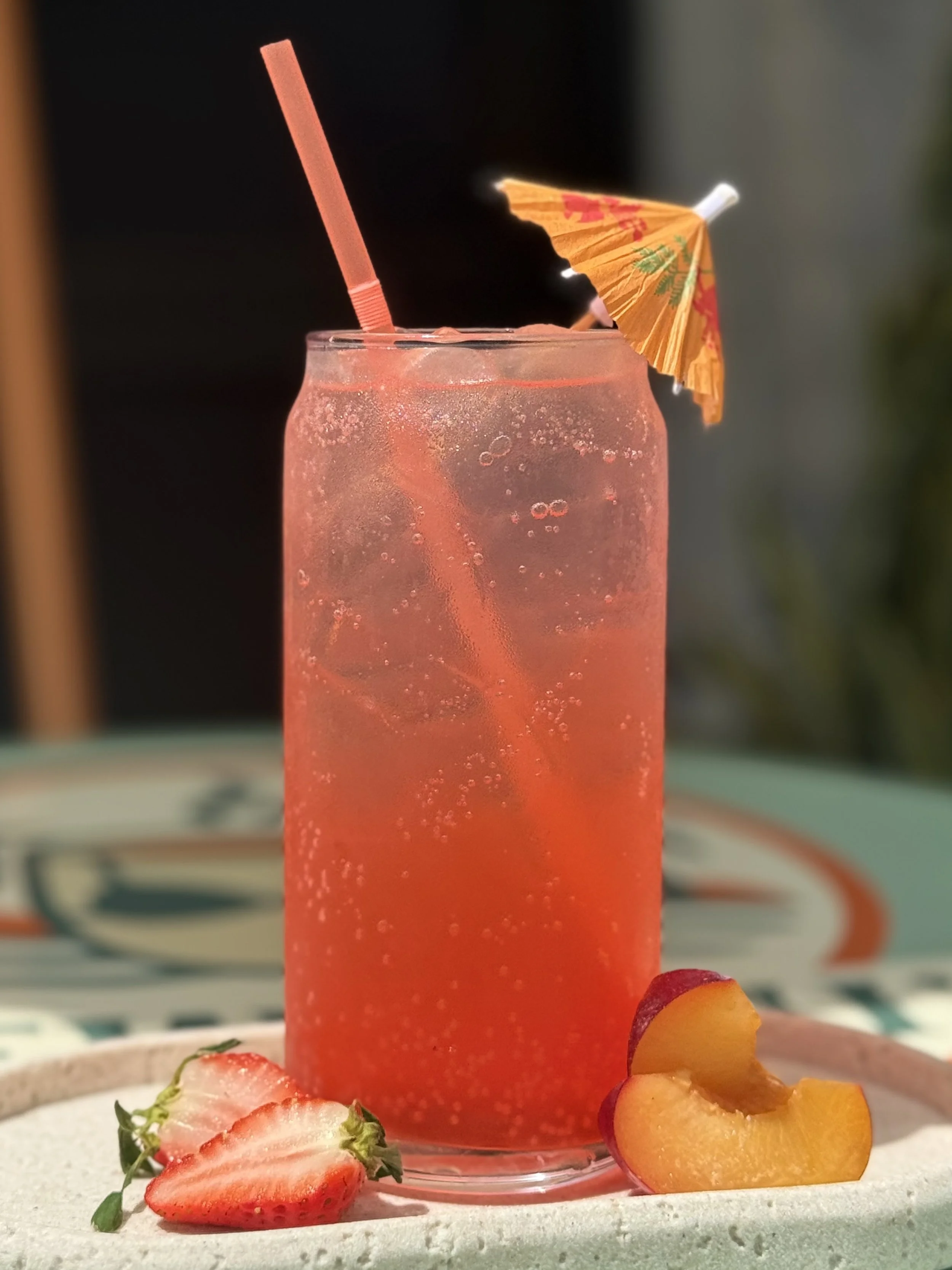 a glass with a refreshing pink lotus wave energy drink flavored strawberry, peach, and guava with a umbrella in it