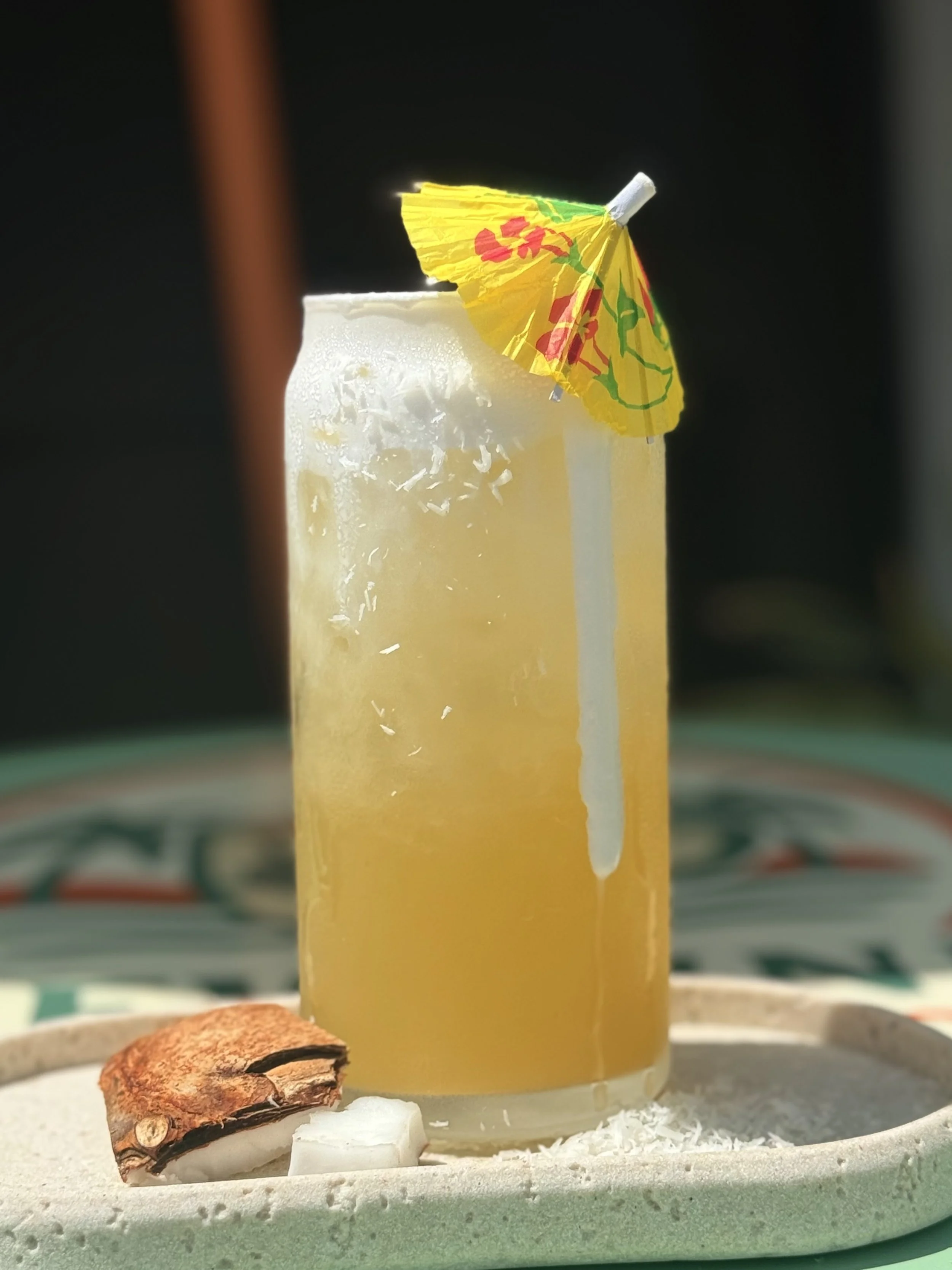 a glass with a refreshing yellow creamy drink of coconut, pineapple, cream, lotus energy mix with a umbrella in it