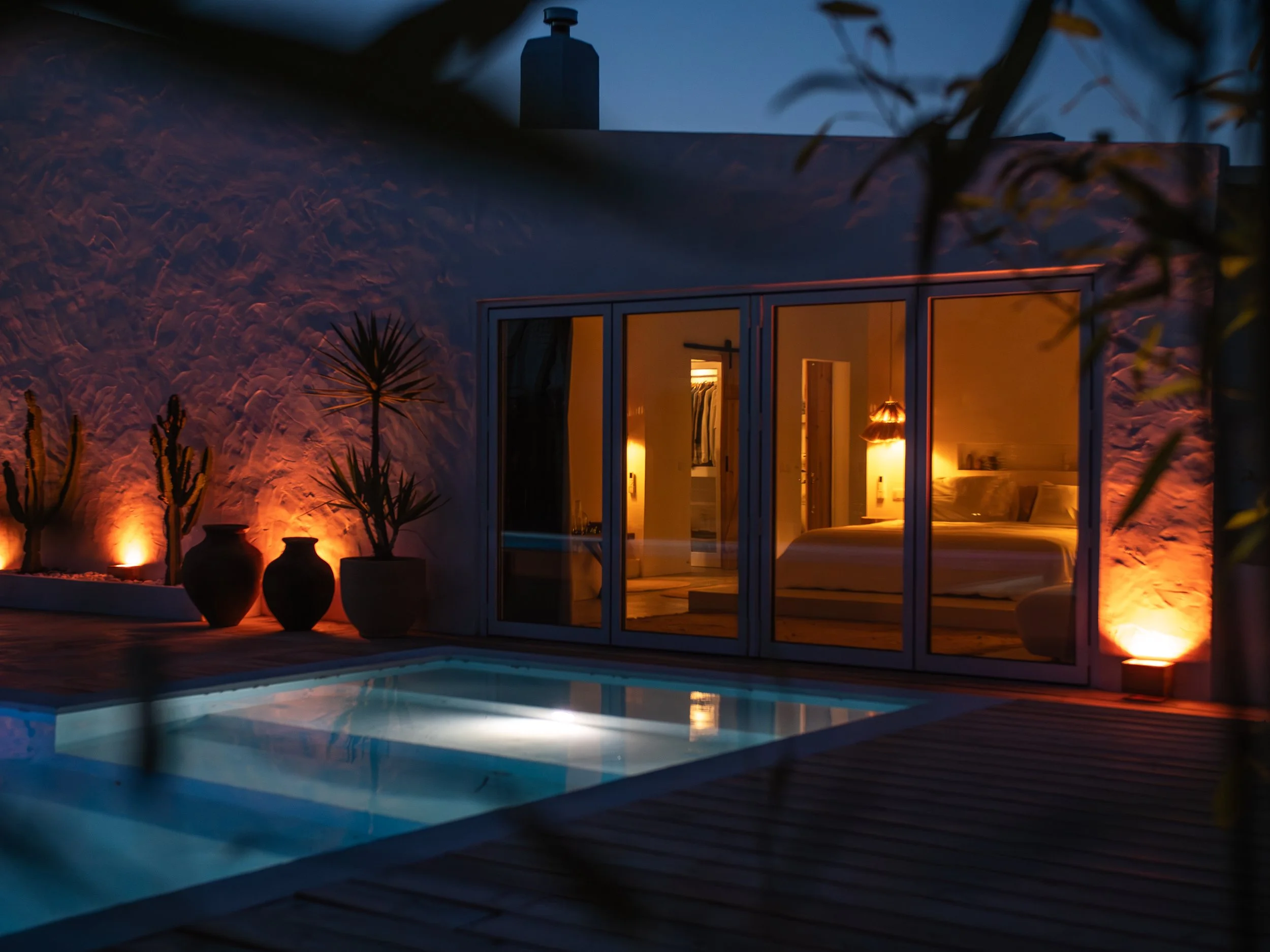 Casa Thala at dusk, a lit bedroom seen through the glass doors beside the heated pool.