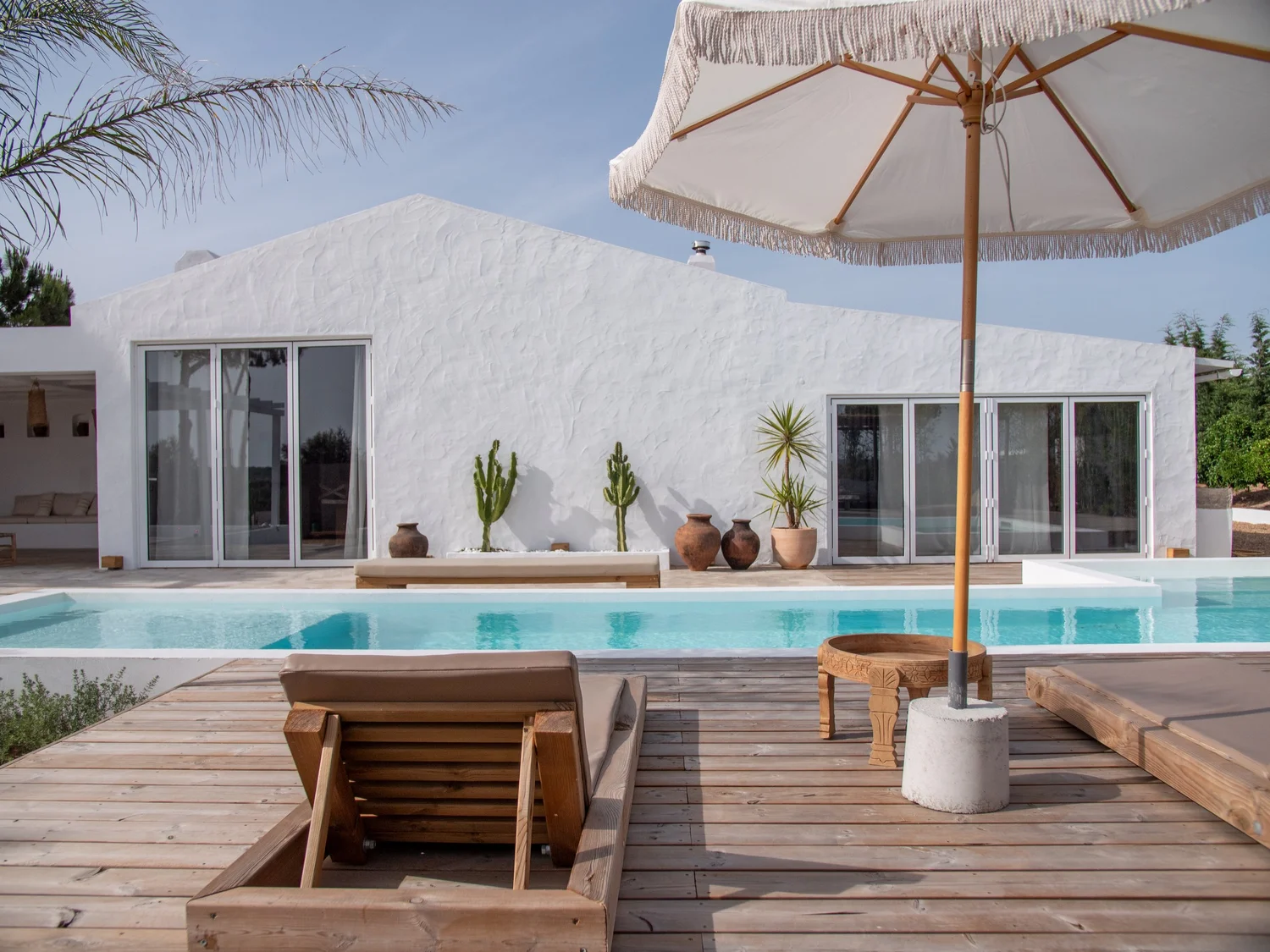 The pool and deck chairs at Casa Thala under a cloudy sky, with cacti and a palm tree.